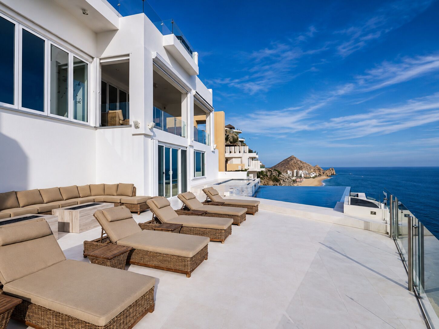 A modern outdoor lounge area with multiple sun loungers and a pool overlooking the ocean.