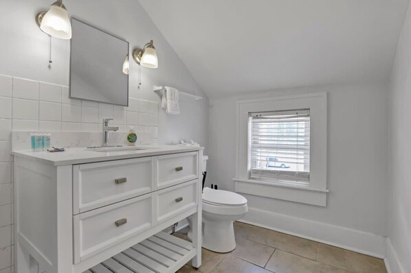 A white bathroom with a vanity, a toilet, and a window.