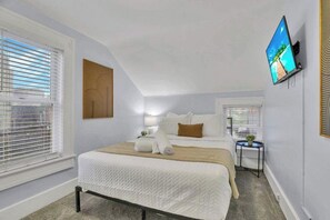 Une chambre à coucher avec un lit, un téléviseur fixé au mur et une fenêtre avec des stores.