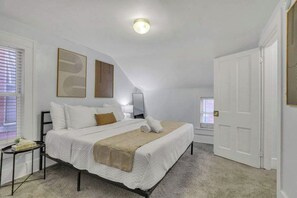 Een slaapkamer met een bed, nachtkastjes, een raam met zonwering en een deur.