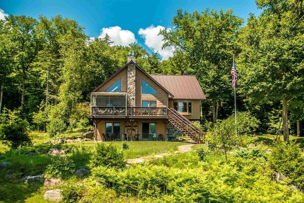 A two-story cabin with a stone chimney, a balcony, and a flagpole.