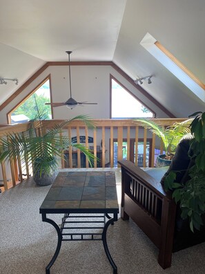 Une pièce mansardée avec un plafond en pente, un ventilateur de plafond, une table avec un banc et des plantes en pot.