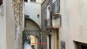 A narrow alleyway with a stone pathway, a small archway, and a door with a chain lock.