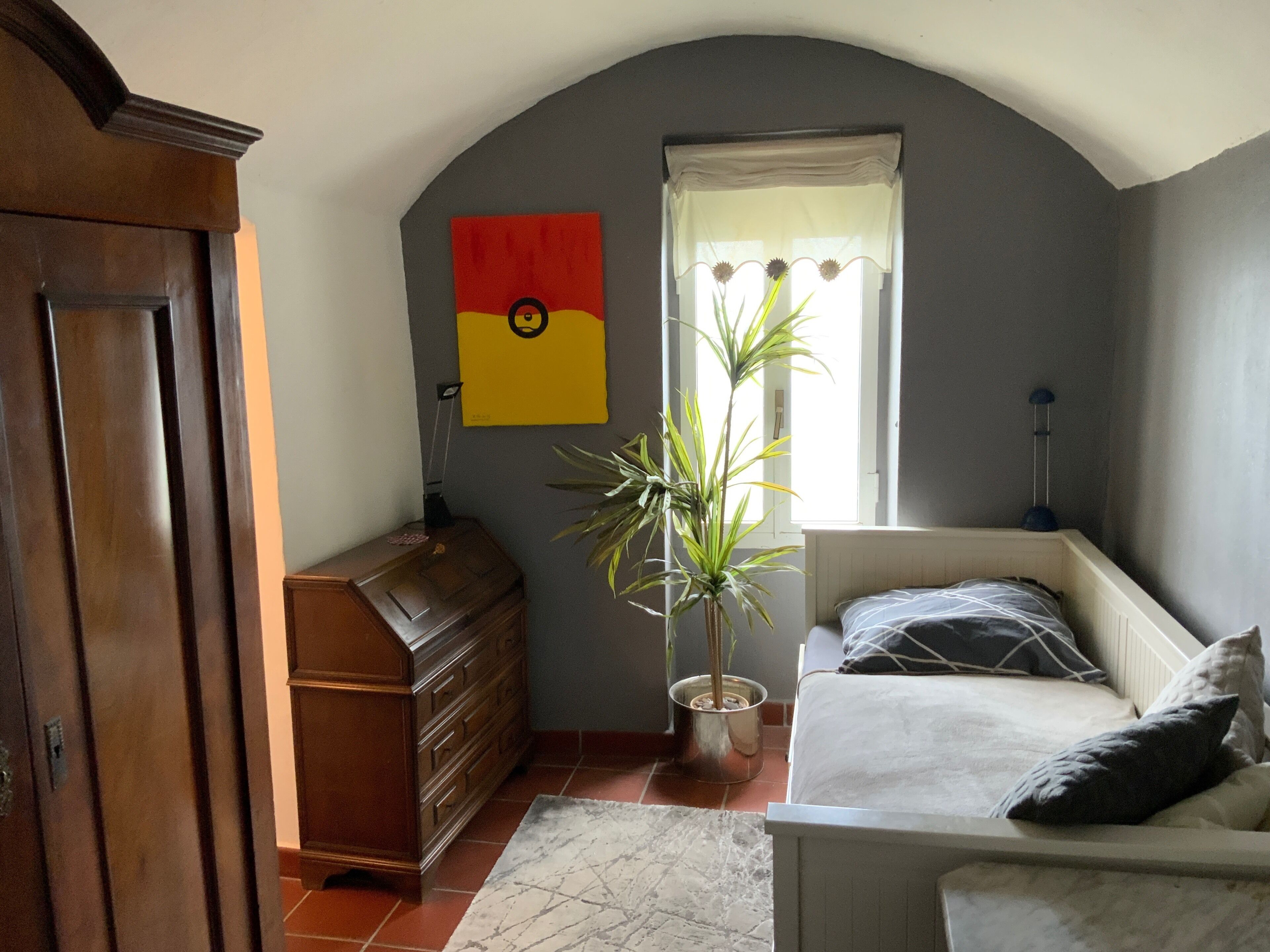 A bedroom with a bed, dresser, potted plant, and a window with curtains.