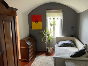 A bedroom with a bed, dresser, potted plant, and a window with curtains.