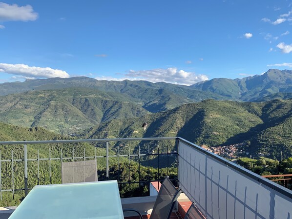 A balcony with a view of green mountains and a town below. - Sun. Wed. Mountains. Family-friendly village house in Liguria, Italy. (Perinaldo)