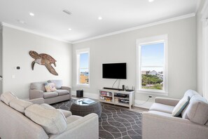 A living room with a sofa, armchairs, a coffee table, a flat-screen TV, and a bookshelf.