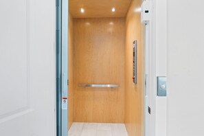 An elevator with a wooden interior, a metal handrail, and a control panel on the wall.