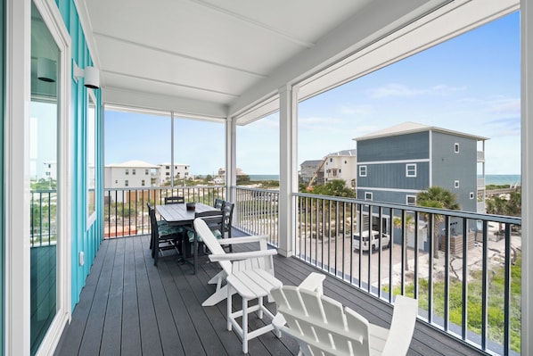 A covered outdoor area with a table and chairs, a view of buildings and the beach.