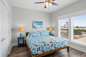 A bedroom with a bed, two bedside lamps, a ceiling fan, a window with blinds, and a view of the outdoors.