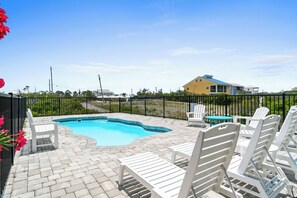 A swimming pool with lounge chairs and a table, surrounded by a fence and greenery.