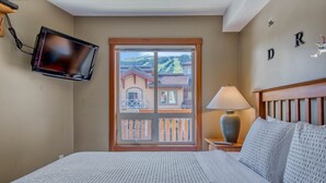 Een hotelkamer met een bed, een aan de muur bevestigde televisie, een raam met uitzicht op huizen en een lampje op het nachtkastje.