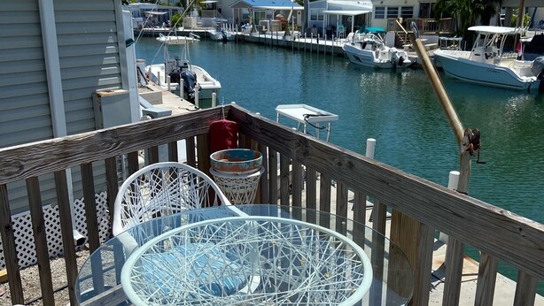 A deck with a glass-top table and white wicker chairs, overlooking a marina with boats and palm trees. - Relaxing and Inviting home in gated community with 35' Seawall Private Dock (Cudjoe Key)