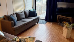 A living room with a sofa, a television, and a balcony with a view. - Relaxing and Inviting home in gated community with 35' Seawall Private Dock (Cudjoe Key)