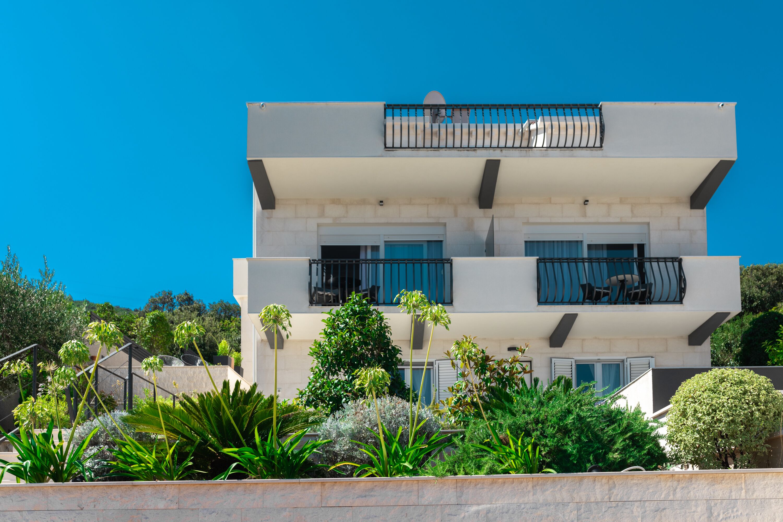 Un immeuble moderne à plusieurs étages, doté de balcons et entouré d’une végétation luxuriante.