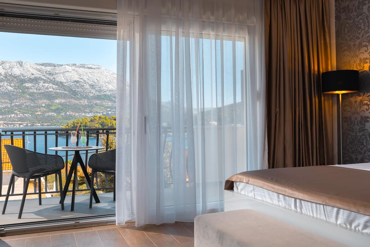 Ein Hotelzimmer mit Balkon, einem Bett, einem Tisch mit Stühlen und Blick auf Berge.
