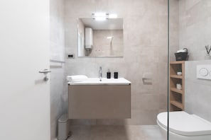A modern bathroom with a built-in sink, a toilet, and a glass shower enclosure. - WISH Apartments (Korcula)