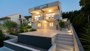 A modern two-story building with balconies, a central entrance, and a landscaped area with steps leading up to the entrance. - WISH Apartments (Korcula)