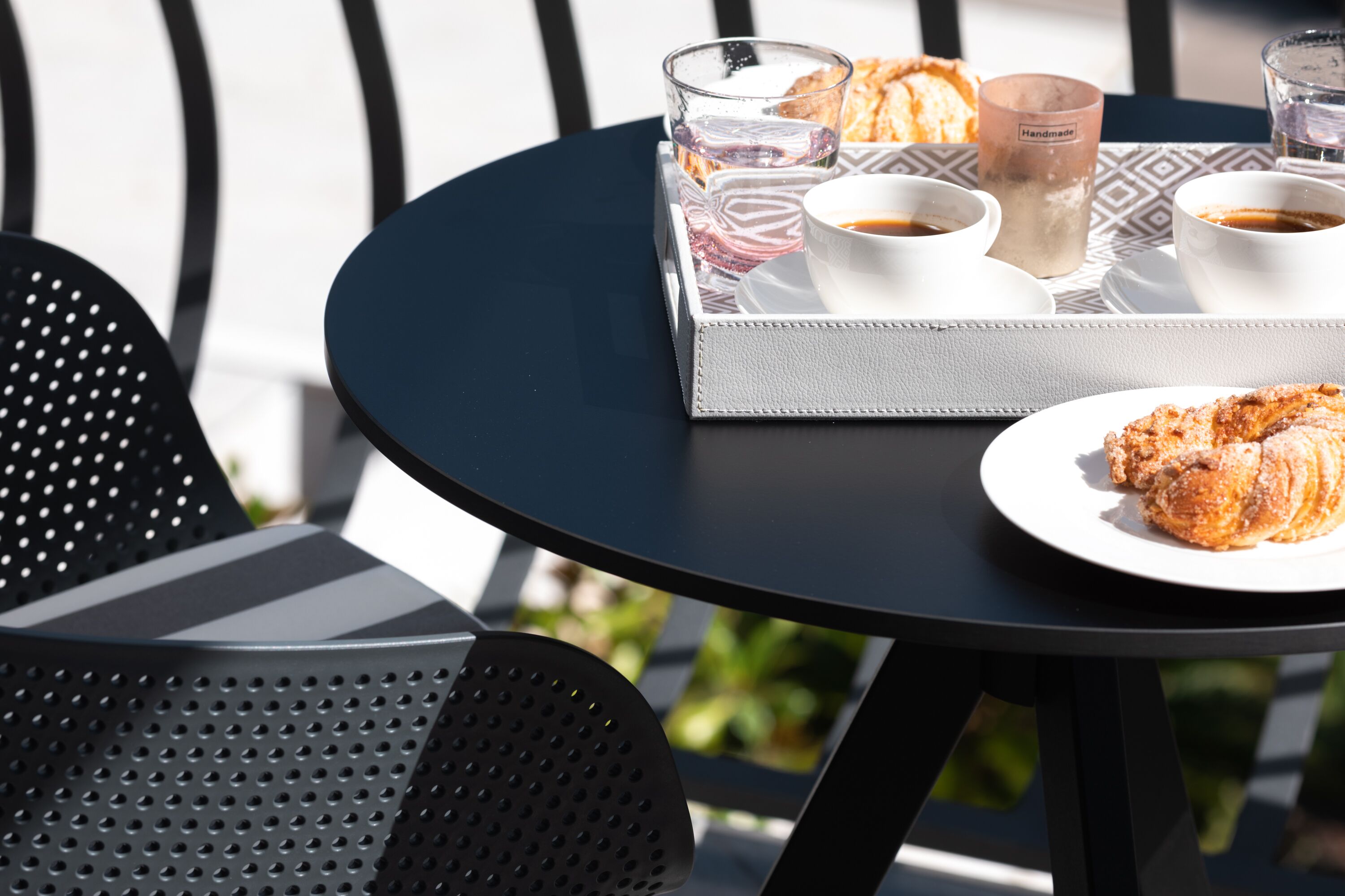 A round table with a tray of pastries, cups of coffee, and glasses of water.