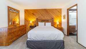 A bedroom with a wooden headboard, a large bed, a dresser with drawers, two bedside tables with lamps, and a mirror on the wall.