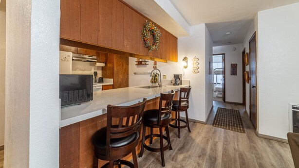 A kitchen with wooden cabinets, a white countertop, and a bar area with four stools.
