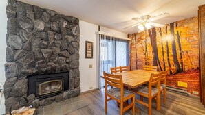 A dining area with a stone wall, fireplace, wooden table, and chairs.