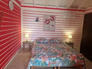 Un dormitorio con una cama, dos mesitas de noche, aire acondicionado de pared y una pared con rayas rojas.