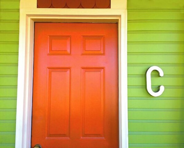 A red door with a white frame, set in a green wall with a large white letter 'C' to the right.