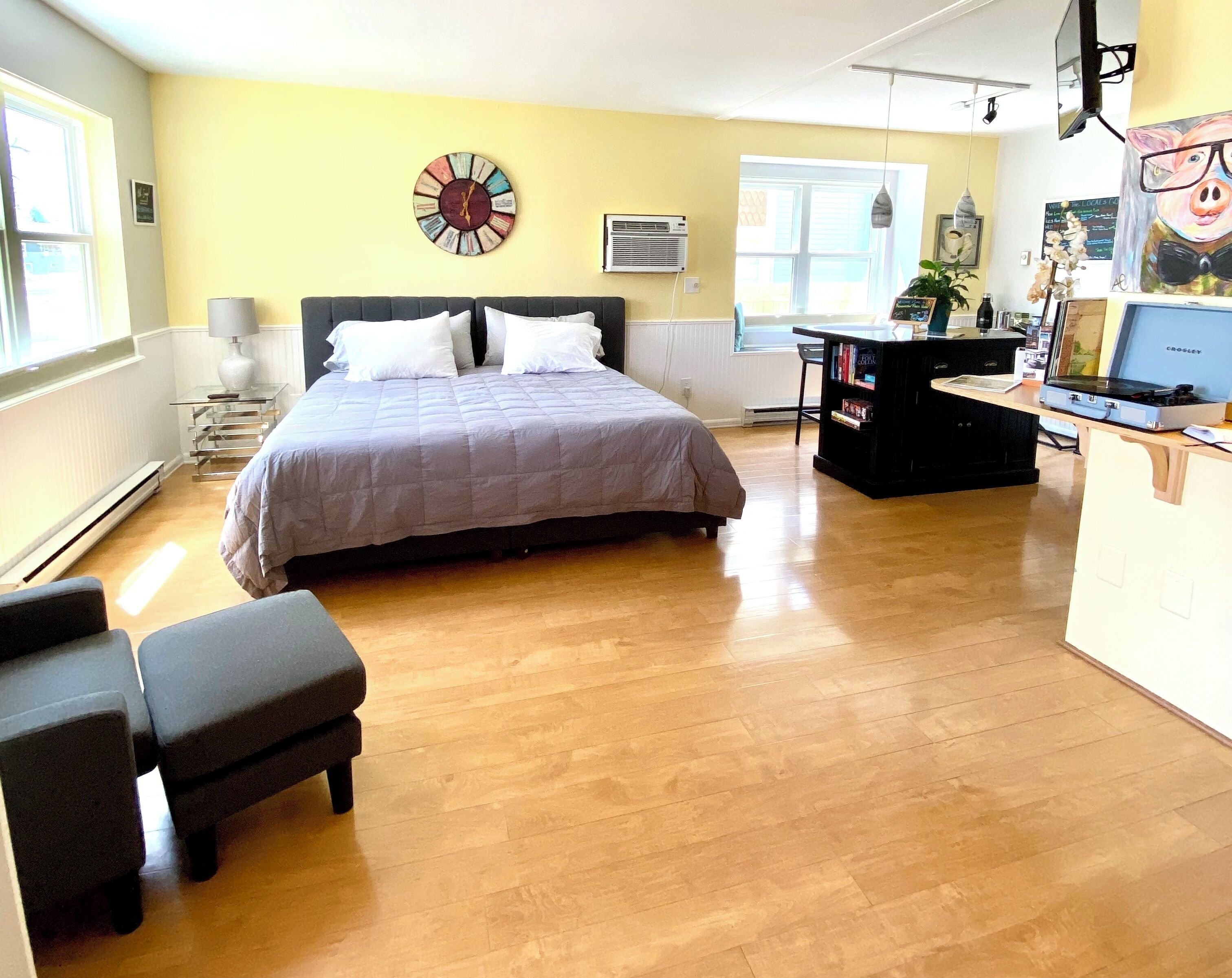 A bedroom with a bed, bedside table, lamp, and a desk with a computer and books.