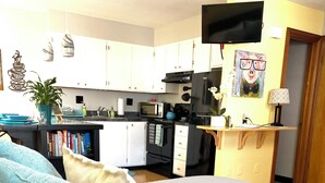 Un dormitorio con una cama, un televisor montado en la pared y una zona de cocina al fondo.