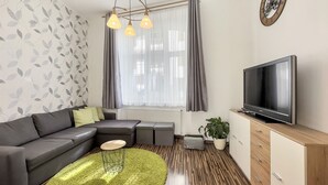 Ett modernt vardagsrum med en grå soffa, en grön matta, en tv och ett träskåp.