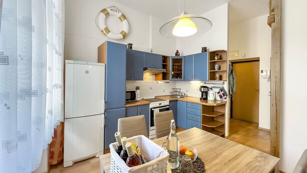 Ett modernt kök med blå skåp, ett vitt kylskåp och ett matbord dekorerat med en korg full av flaskor och frukt.