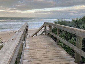 A wooden boardwalk leading to a beach with a cloudy sky. - Beach Breeze - Oceanwalk Resort 14-206 (New Smyrna Beach)