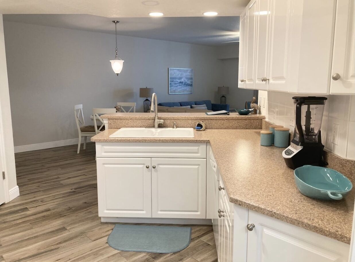 A modern kitchen with white cabinets, a granite countertop, and a blue rug.