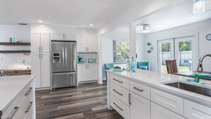 A modern kitchen with white cabinetry, a stainless steel refrigerator, a built-in oven, and a large island with a sink.