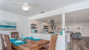 A modern kitchen with white cabinets, a central island, and a dining area with wooden chairs and blue tableware.