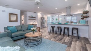A modern kitchen with a central island, bar stools, and a ceiling fan.