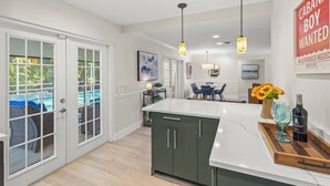 A modern kitchen with a large island, a dining area with a table and chairs, and a view of a pool through a glass door. - Toes in the Water - Pool Home on Siesta Key (Siesta Key)