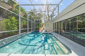 An indoor swimming pool with clear water, surrounded by glass walls and a metal frame structure.