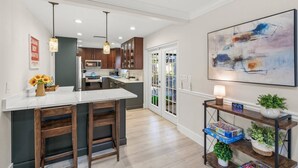 A modern kitchen with a central island, dark wooden cabinets, and a large abstract painting on the wall. - Toes in the Water - Pool Home on Siesta Key (Siesta Key)