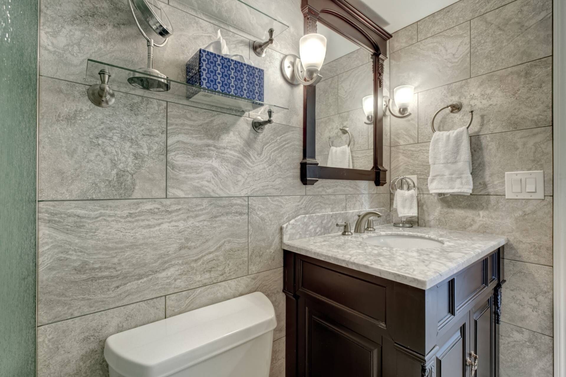 A bathroom with a marble sink, a toilet, a mirror, and a towel rack.