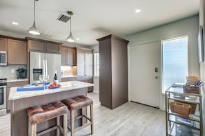A modern kitchen with wooden cabinets, a marble countertop, and a central island with stools. - Bay Tree Beach Side (Siesta Key)