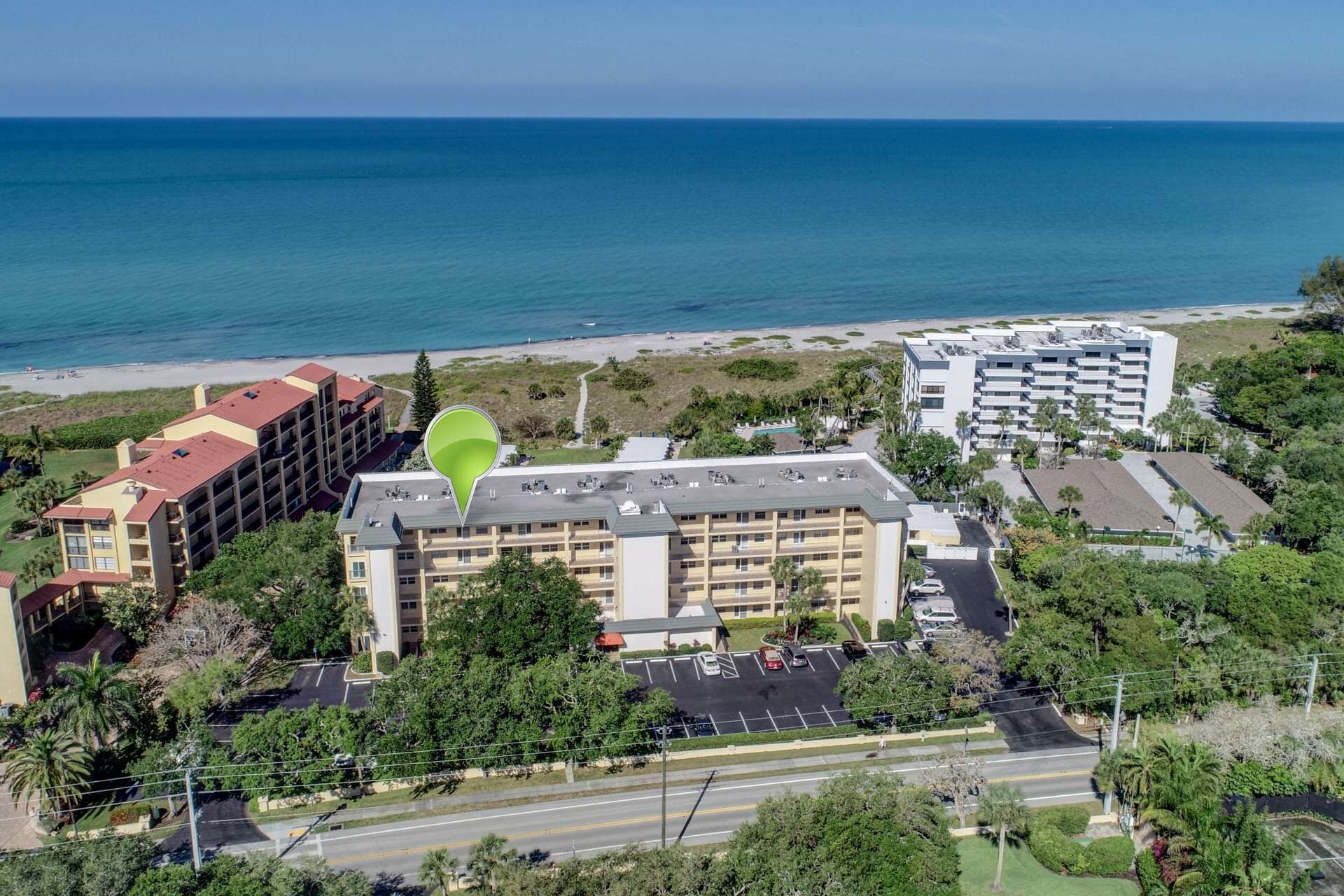 An aerial view of a hotel with multiple floors, a parking lot, and a beach in the background.