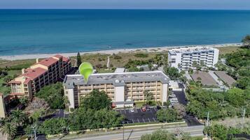 An aerial view of a hotel with multiple floors, a parking lot, and a beach in the background.
