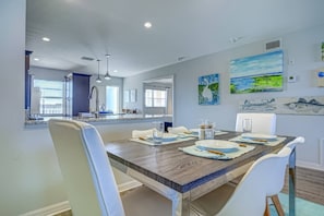 A modern dining area with a wooden table, white chairs, and a kitchen in the background. - Bay Tree Beach Side (Siesta Key)
