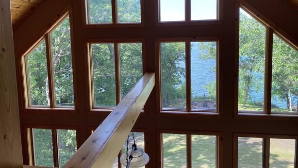 Ein Zimmer mit großen Fenstern und Holzbalkendecke, mit Blick auf Bäume und ein Gewässer.