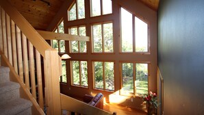 Ein geräumiges Zimmer mit großen Fenstern, einer Holztreppe und Blick ins Freie.