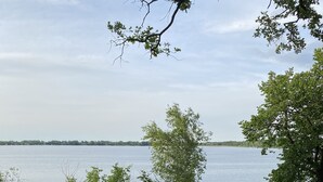 Ein runder Feuerkorb, umgeben von Bänken und einem Tisch, auf einer gepflasterten Fläche mit Blick auf einen See.