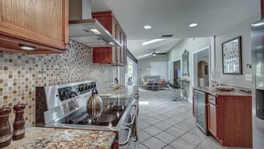 A modern kitchen with a stainless steel stove, wooden cabinets, and a tiled backsplash. - Canopy Cottage on Siesta Key (Siesta Key)