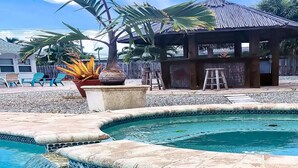Une piscine dont le bord est orné de mosaïques, entourée d’une plage de galets et de palmiers.